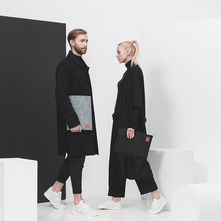 Tunt laptopfodral i svart respektive grå PET-filt. En kvinna och man, båda har svarta kläder och vita sneakers