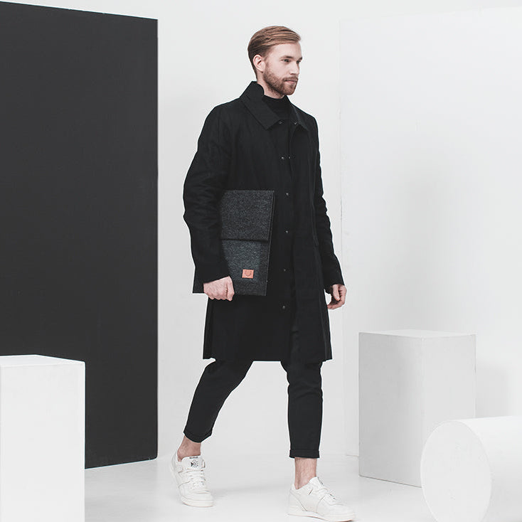 Man med svart rock och vita sneakers håller ett Malmö laptopfodral