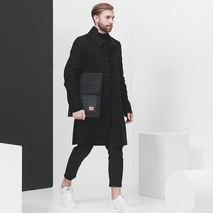 Diskret laptopfodral i PET-filt bärs av en man med svart rock och vita sneakers. 