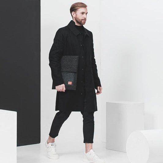 Diskret laptopfodral i PET-filt bärs av en man med svart rock och vita sneakers. 